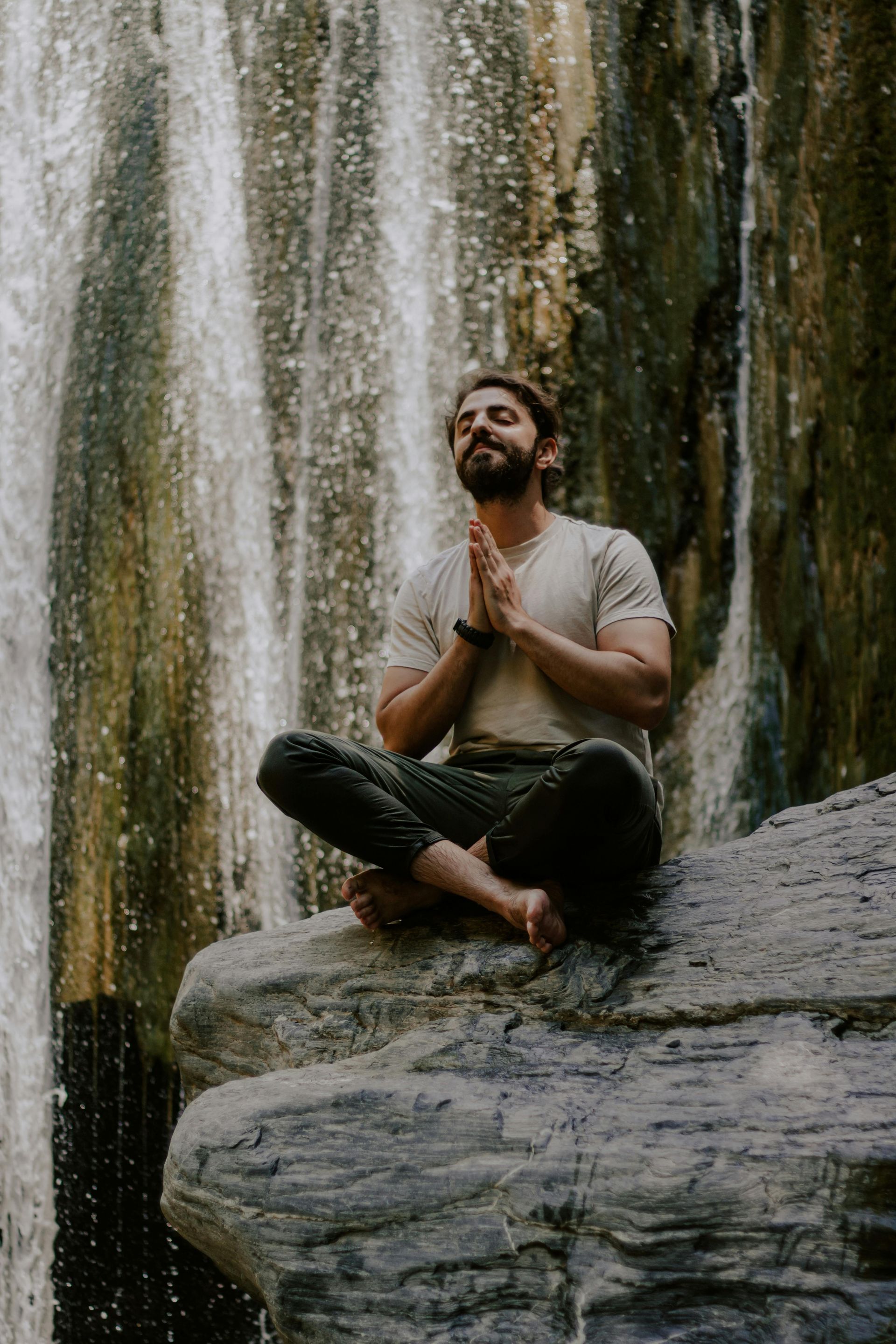 Person meditating on a rock in front of a waterfall