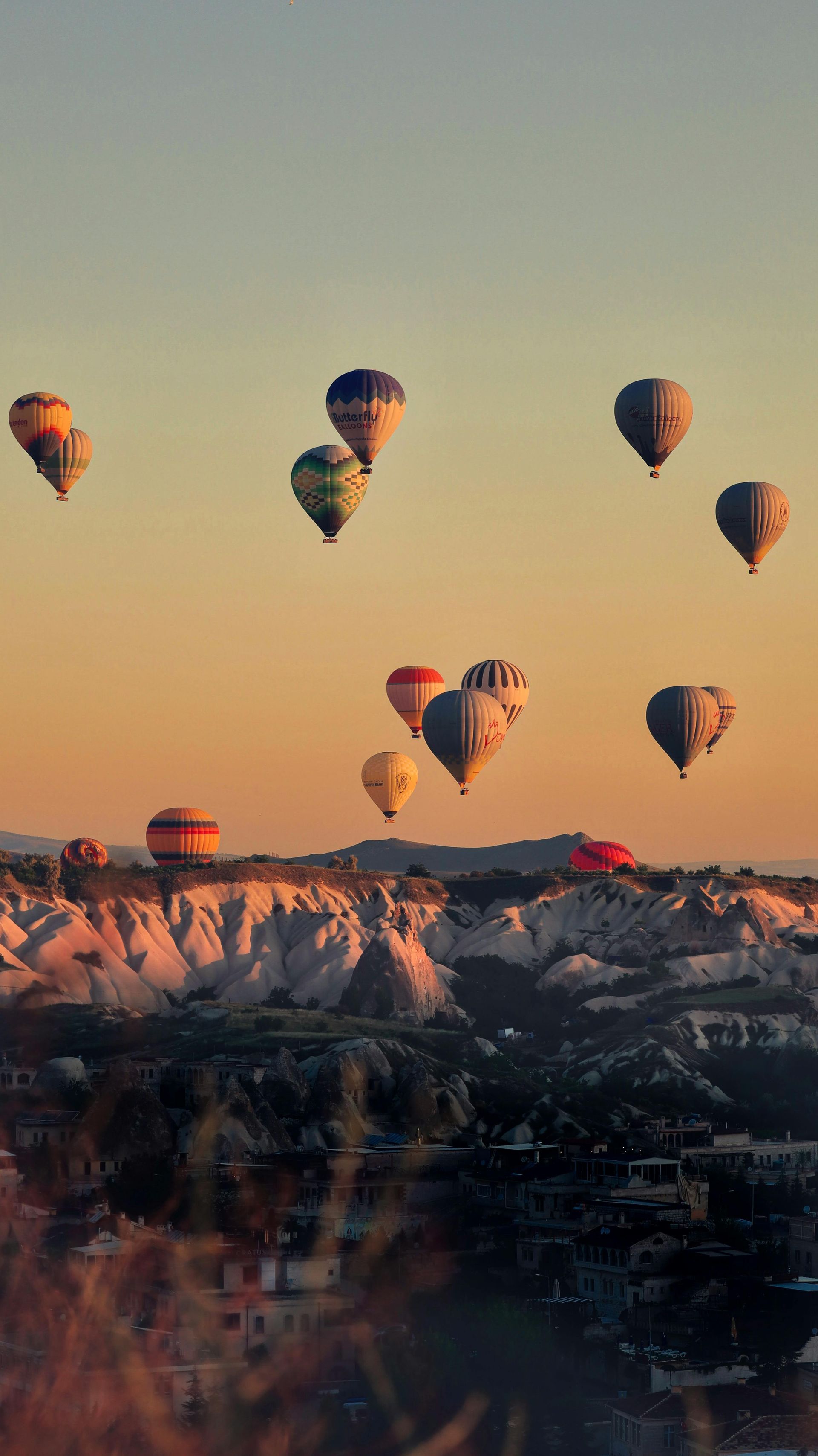 Hot air balloons floating over snowy cliffs at sunrise, with warm orange sky and distant mountains
