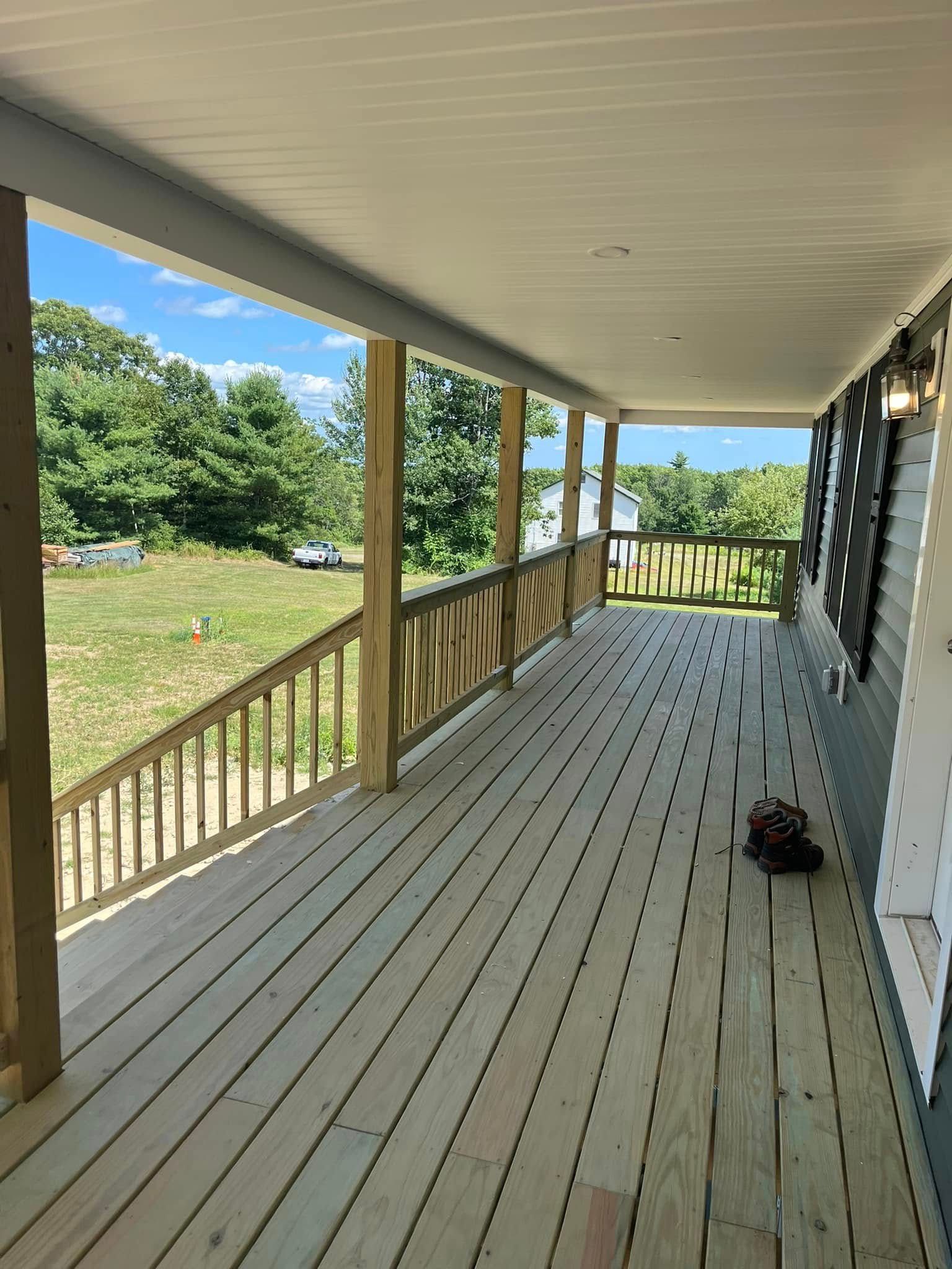 A large wooden porch with a view of a field and trees.