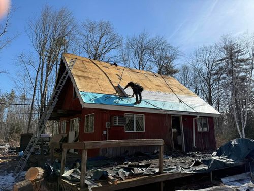 A man is working on the roof of a red house.