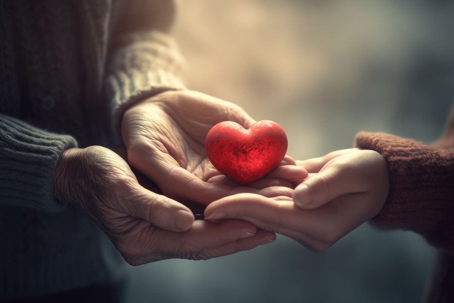 Two pairs of hands meeting to cradle a glowing, bright red heart against a soft, out-of-focus background.