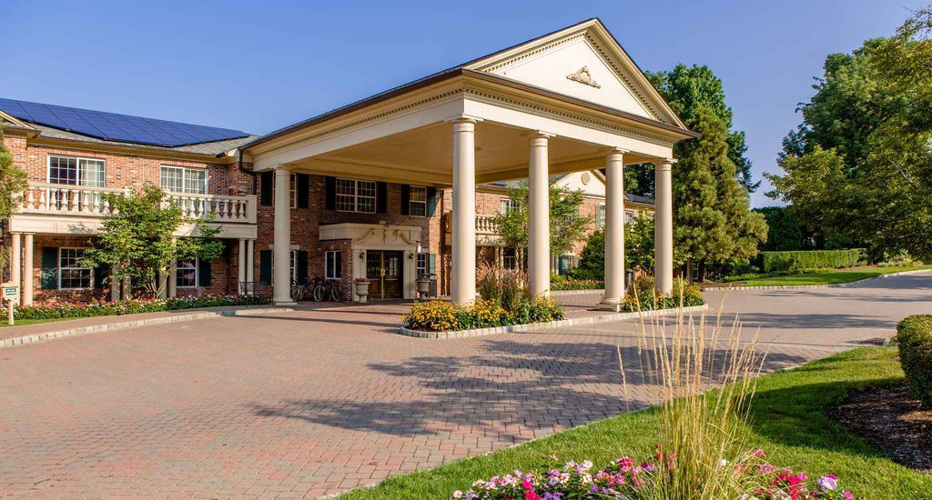 A brick hotel exterior with a large, white-columned portico under a clear blue sky, featuring a paved driveway.