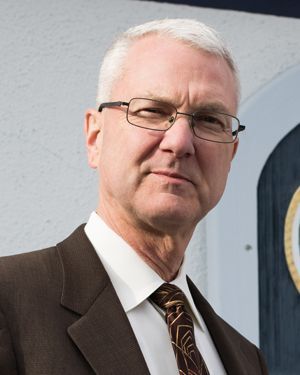 A person with gray hair and glasses wearing a suit and patterned tie, looking directly at the camera.