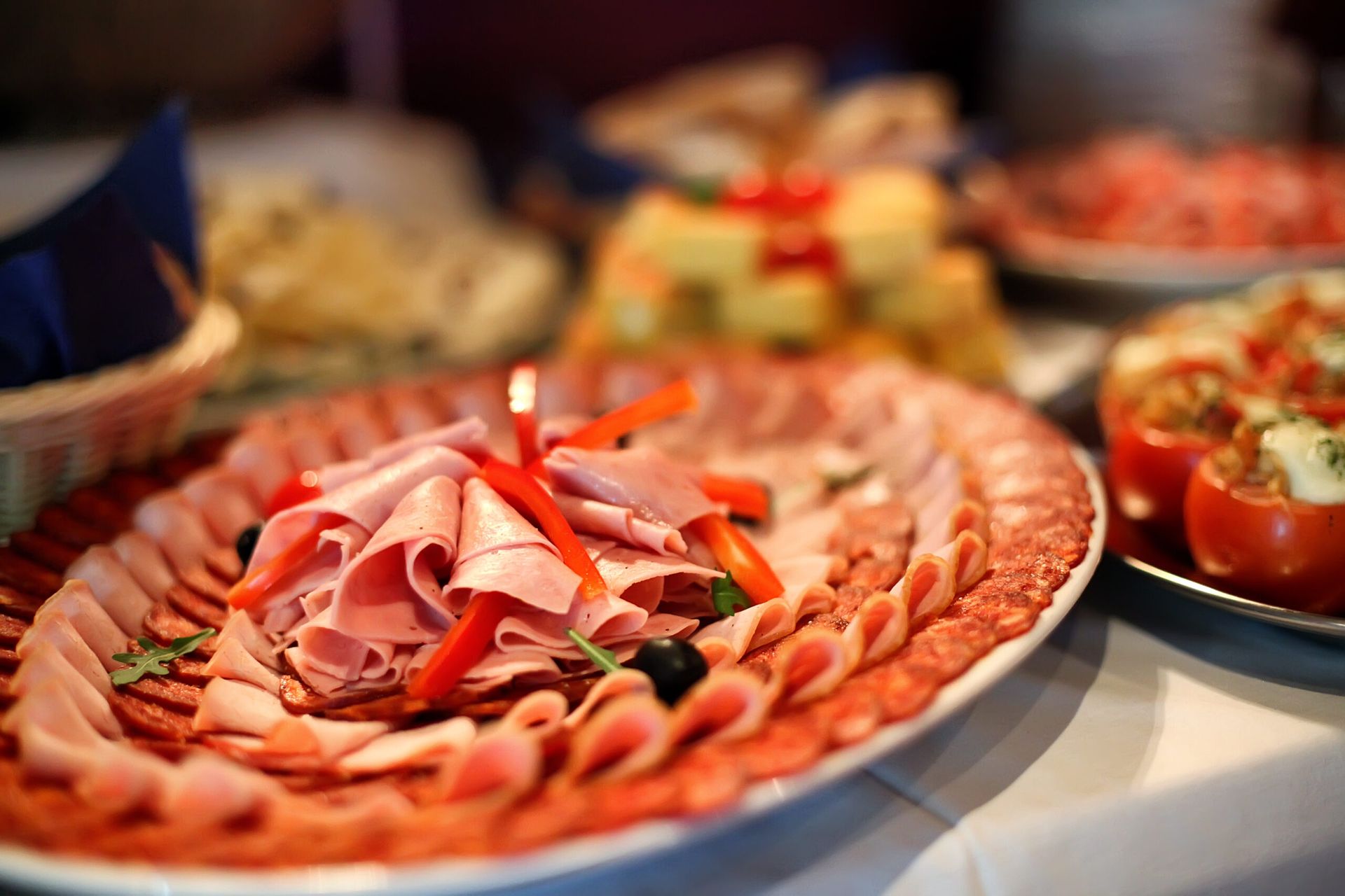 A platter of sliced ham and salami arranged in overlapping layers, garnished with red pepper strips and black olives.