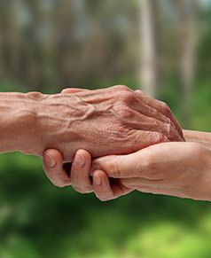 Two hands held together, one gently resting on top of the other, against a soft, out-of-focus green outdoor background.