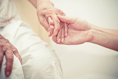 A close-up of a person gently holding an elderly individual’s hand to offer comfort and support.