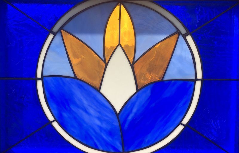 Stained glass panel with a circular design featuring a central white flower petal surrounded by yellow and blue shapes.