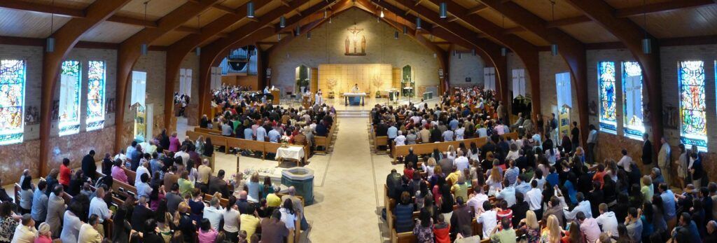 Wide-angle view of a congregation seated in pews inside a large, wooden-beamed church during a service.
