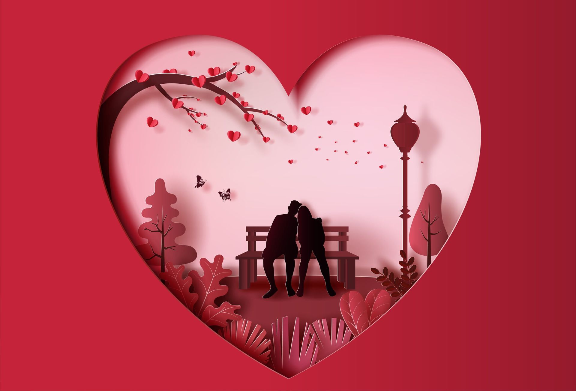 A red paper-cutout heart frame containing the silhouettes of two people sitting on a bench under a tree and streetlamp.