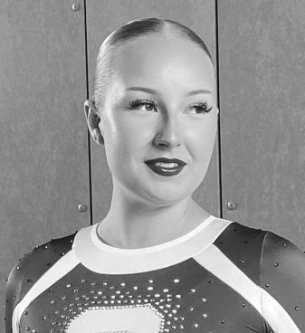 A black and white photo of a woman wearing a cheerleading uniform.