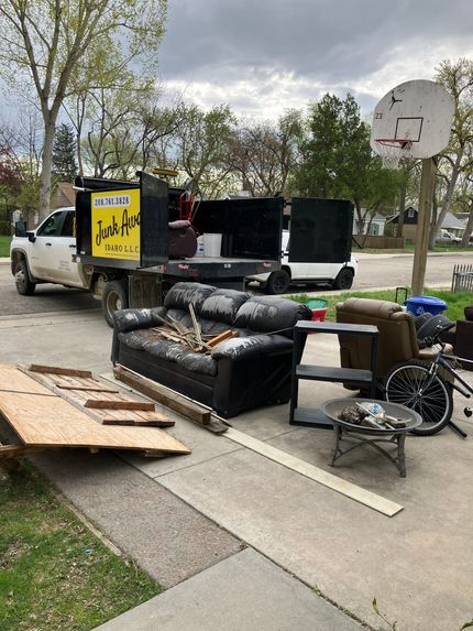 A couch , chair , and wheelchair are sitting on the sidewalk next to a truck.