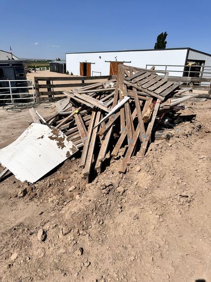 A pile of wood is sitting in the dirt in front of a building.