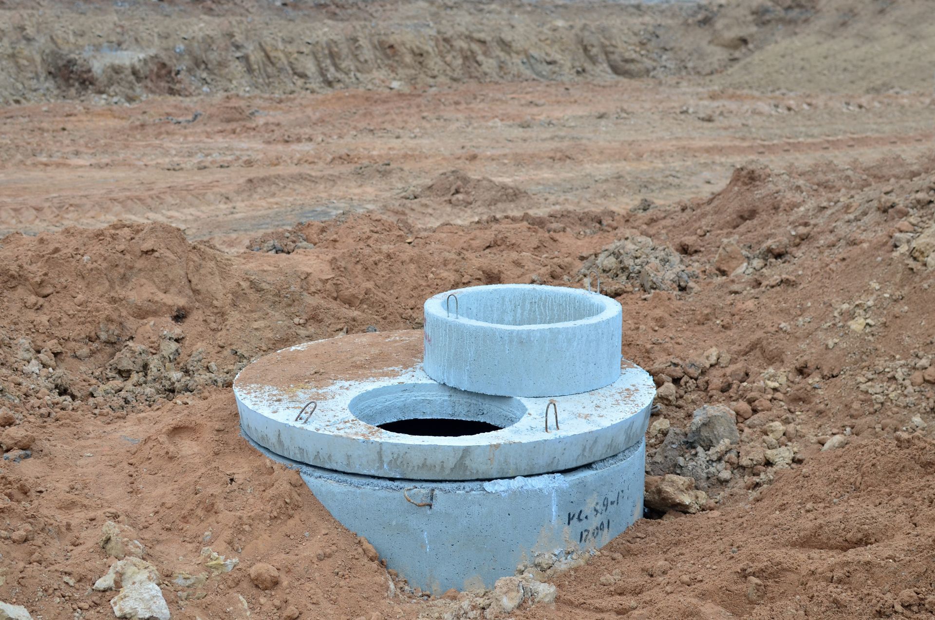 Blue concrete utility structure in a dirt excavation site, with a circular opening and raised pipe section