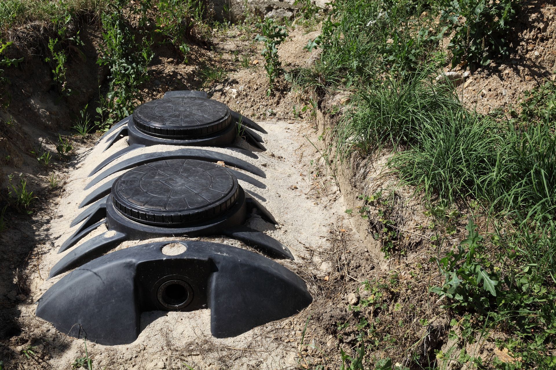 Three black plastic tanks buried in a dirt hillside, with circular lids visible on top.