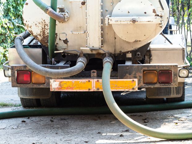 Rear view of a beige vacuum truck with hoses extending onto a wet road