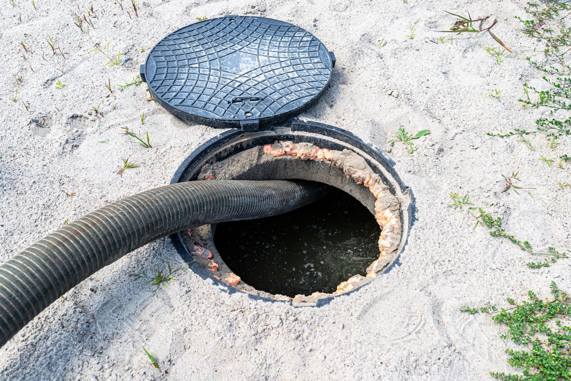 Open manhole with a hose inserted, showing a dark circular opening on concrete pavement.