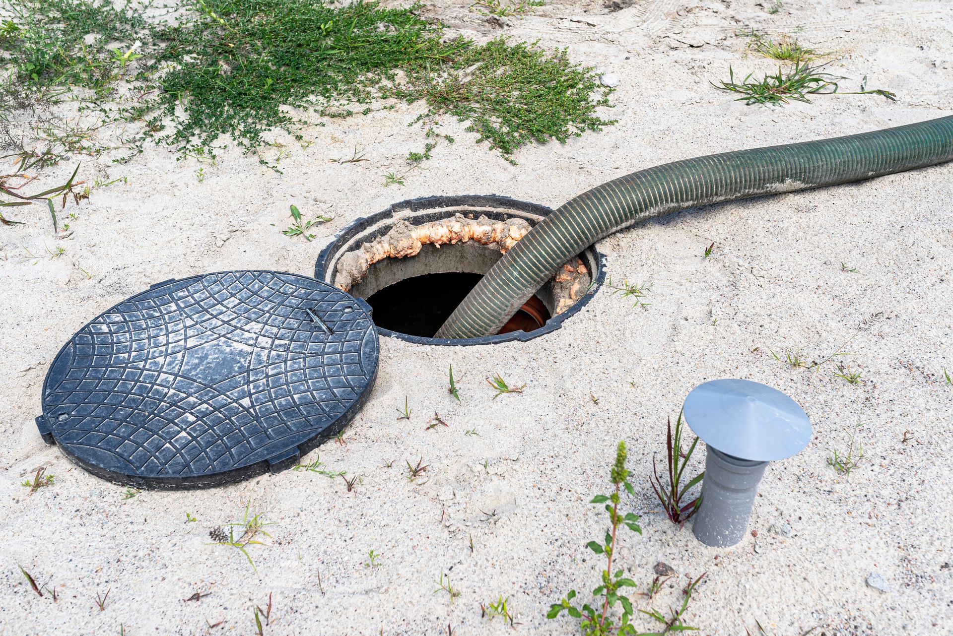 Green hose exiting a hole in the ground beside a blue circular cover on sandy soil