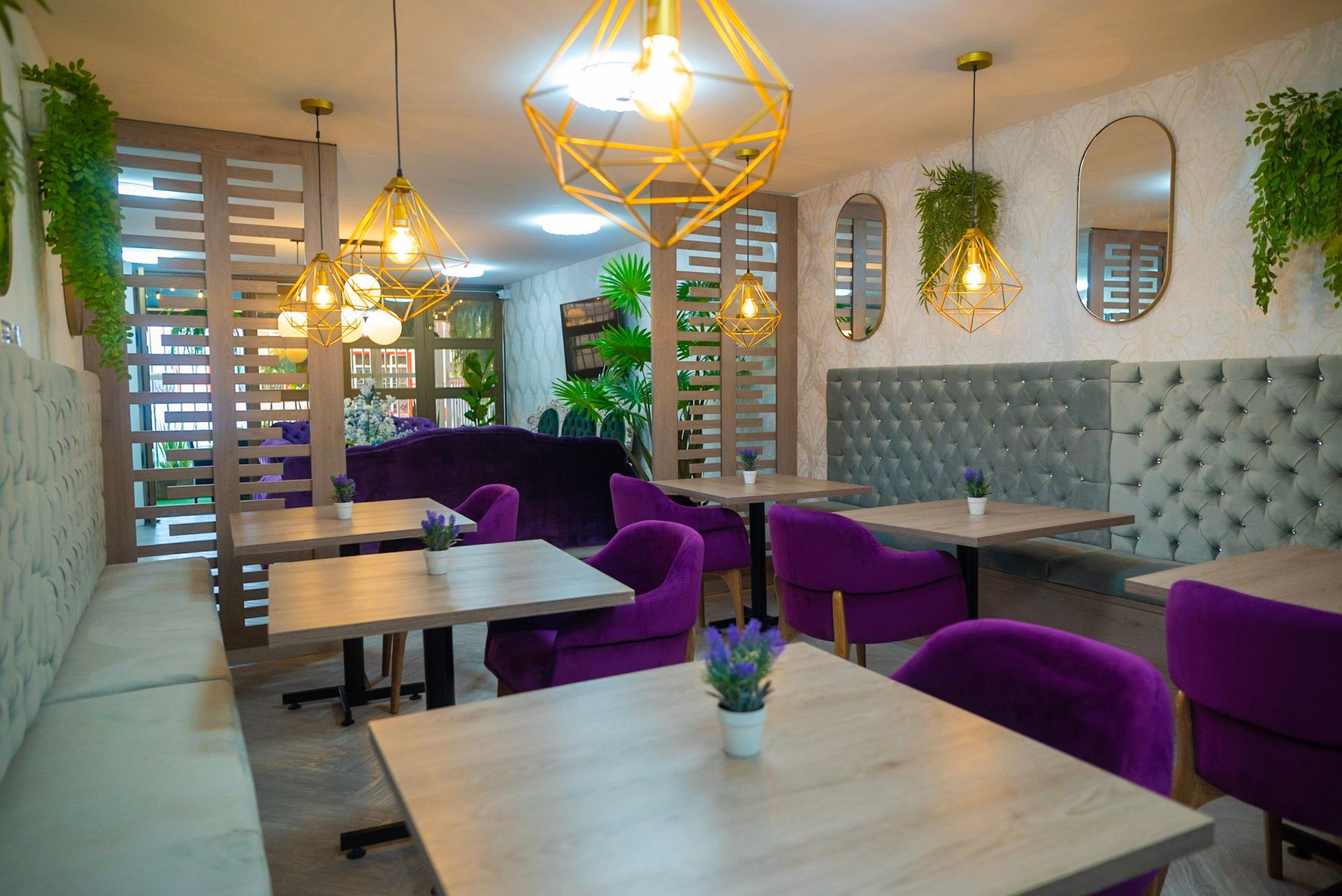 Un interior de cafetería moderno y bien iluminado con mesas de madera clara, sillas tapizadas en color violeta vibrante e iluminación geométrica.