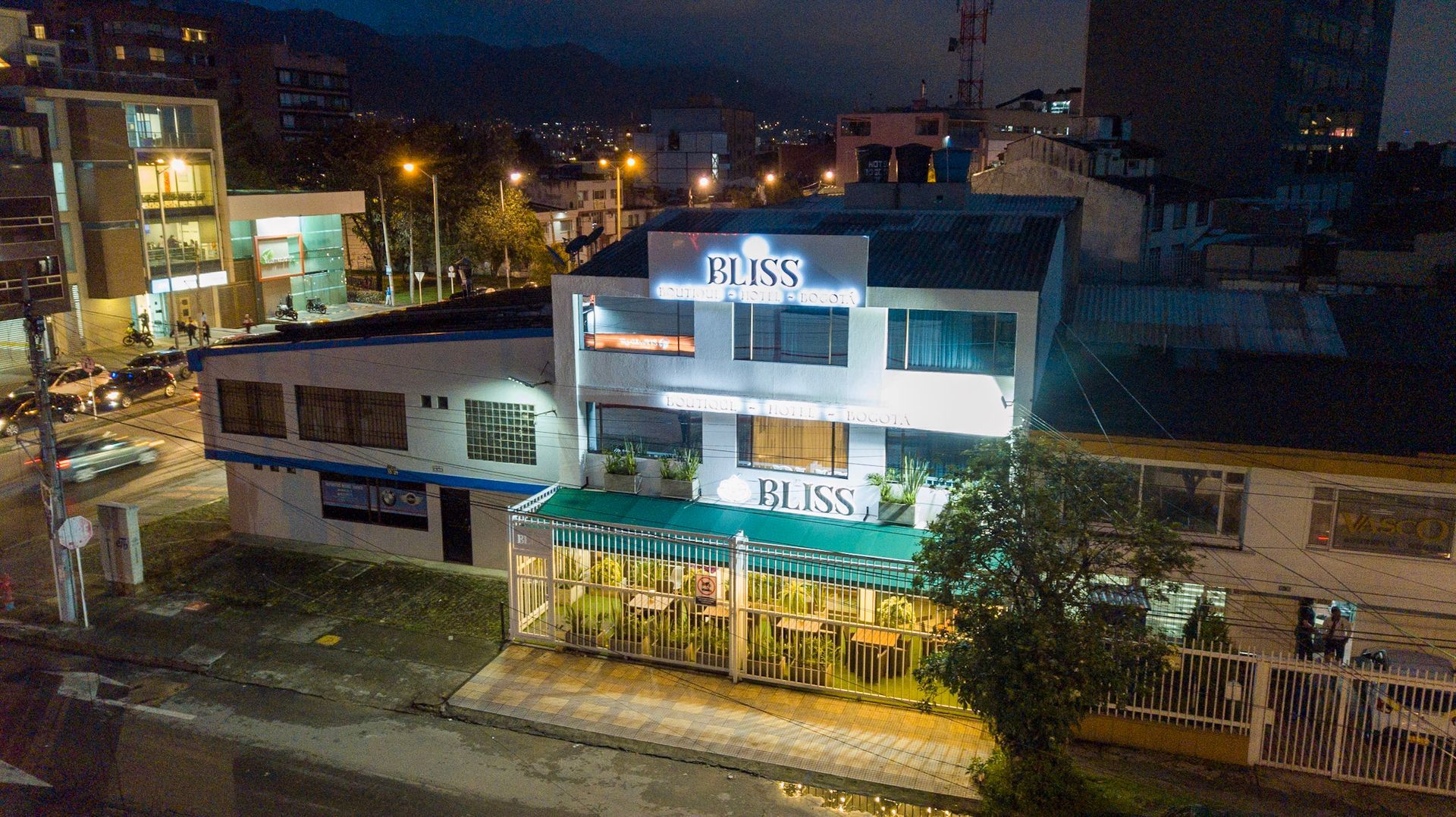 Un edificio iluminado llamado Bliss por la noche, con un patio iluminado en la planta baja con asientos en un entorno urbano.