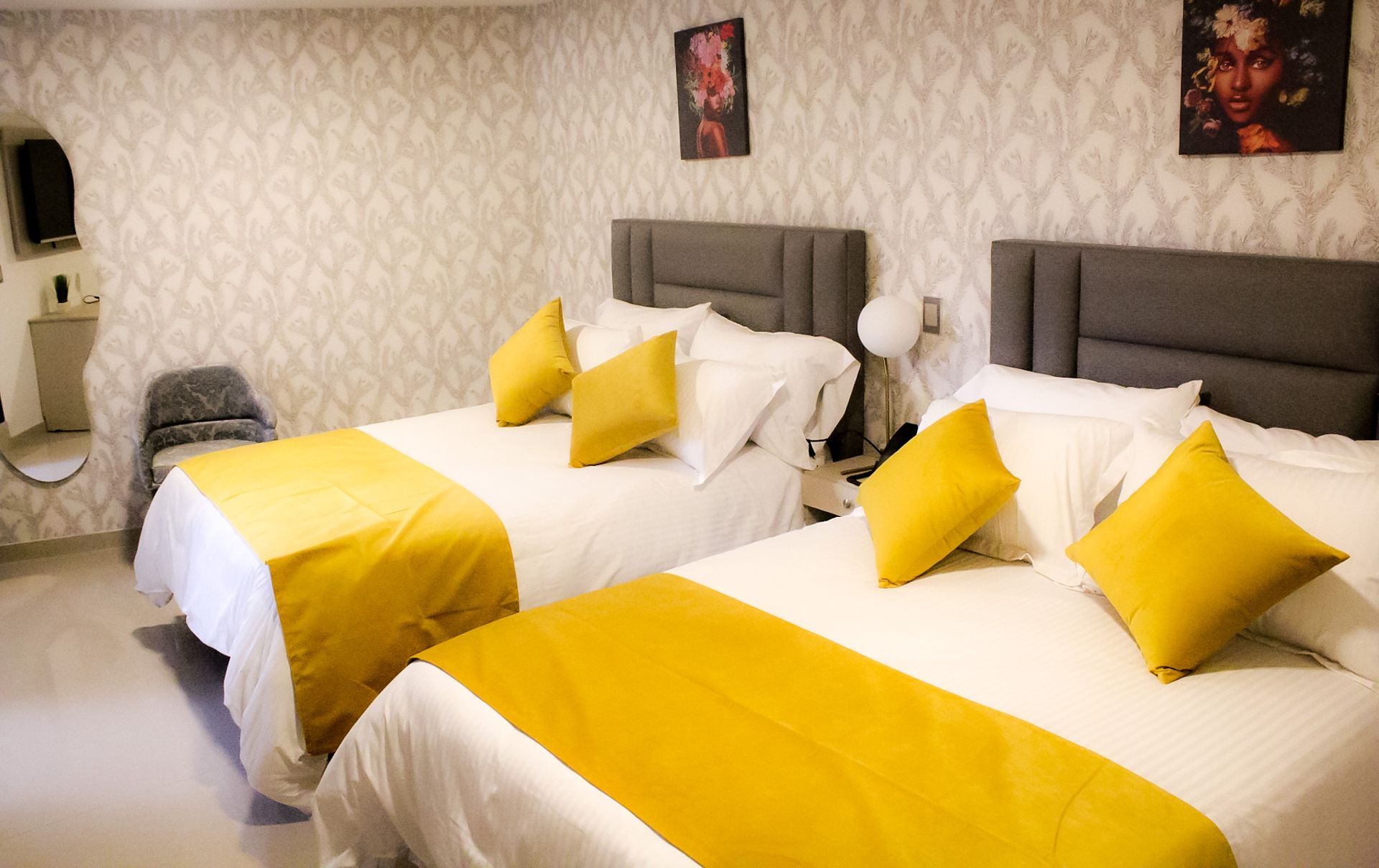 Una habitación de hotel con dos camas con ropa de cama blanca, mantas amarillas y almohadas decorativas amarillas a juego sobre cabeceras grises.