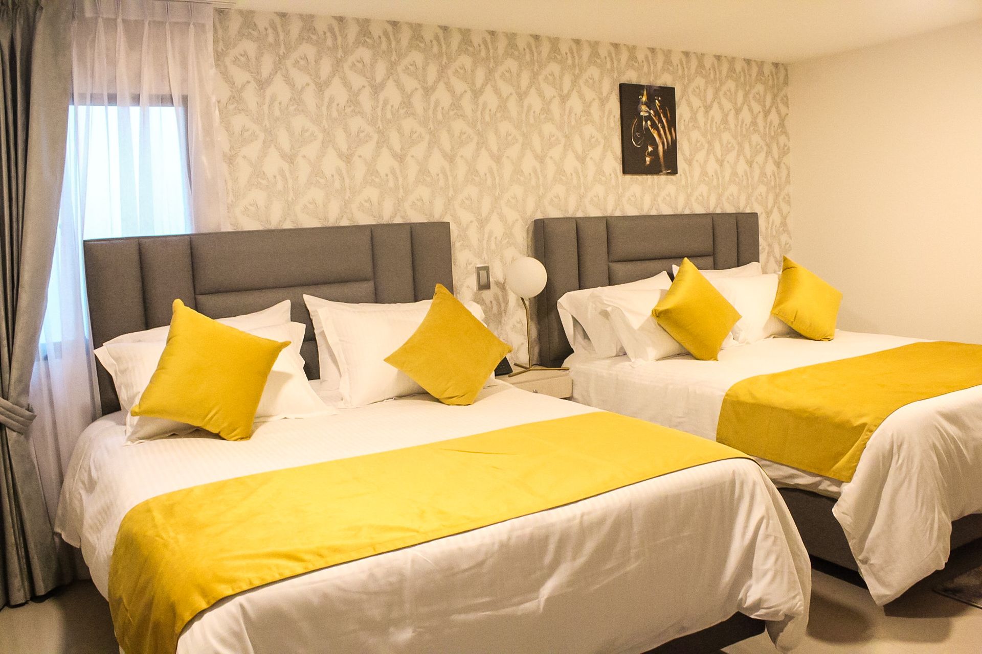 Un dormitorio con dos camas con ropa de cama blanca, almohadones y corredores con detalles en amarillo, contra una pared con papel tapiz estampado.