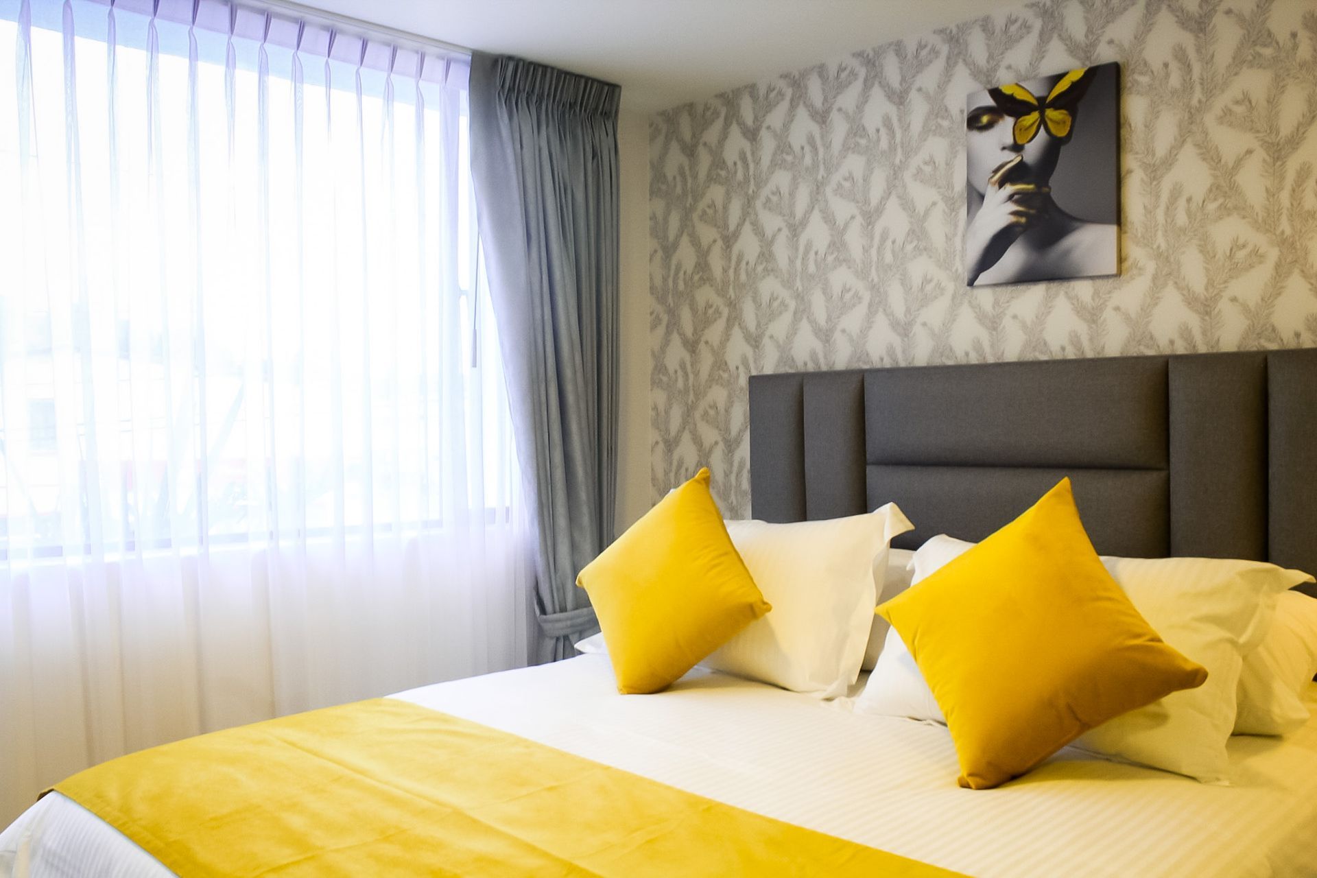 Un dormitorio de hotel con una cama cubierta con sábanas blancas y almohadas de color amarillo brillante, sobre un papel tapiz estampado.