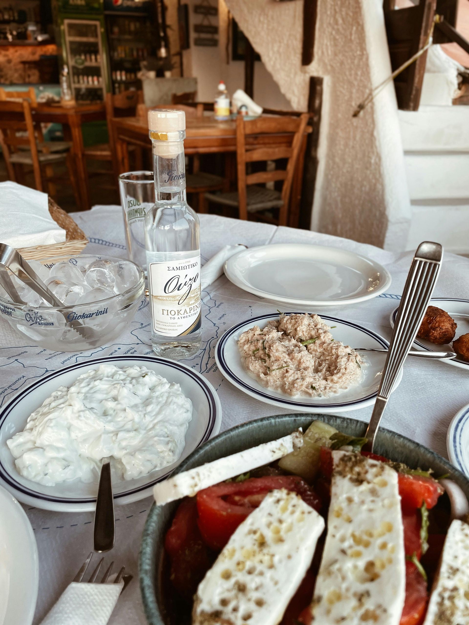 Una ensalada griega con queso feta, tzatziki y una botella de raki en la mesa de un restaurante.