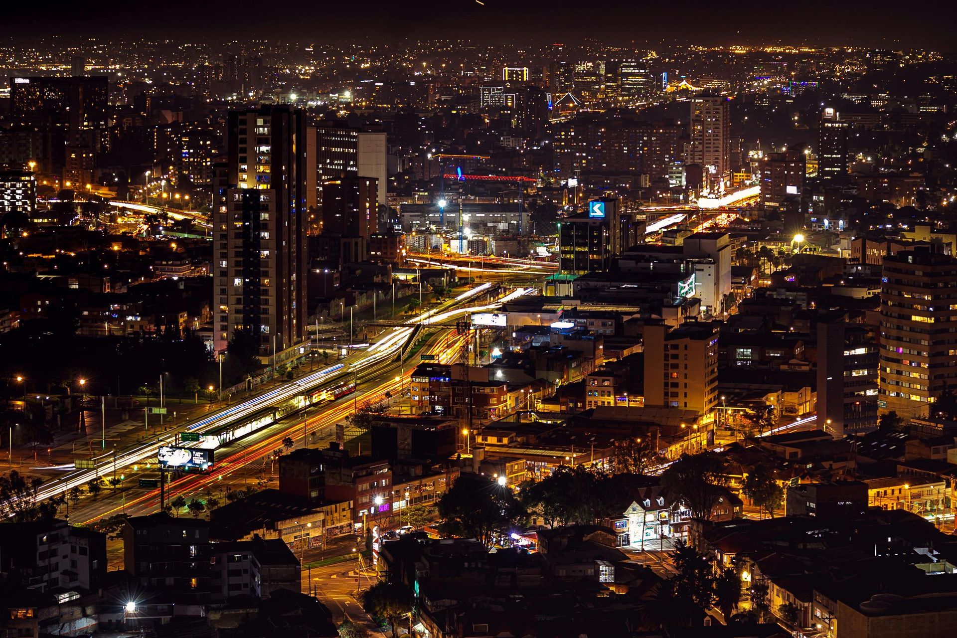 Una vista nocturna desde un ángulo alto de un horizonte urbano brillante con edificios iluminados y una autopista con mucho tráfico.