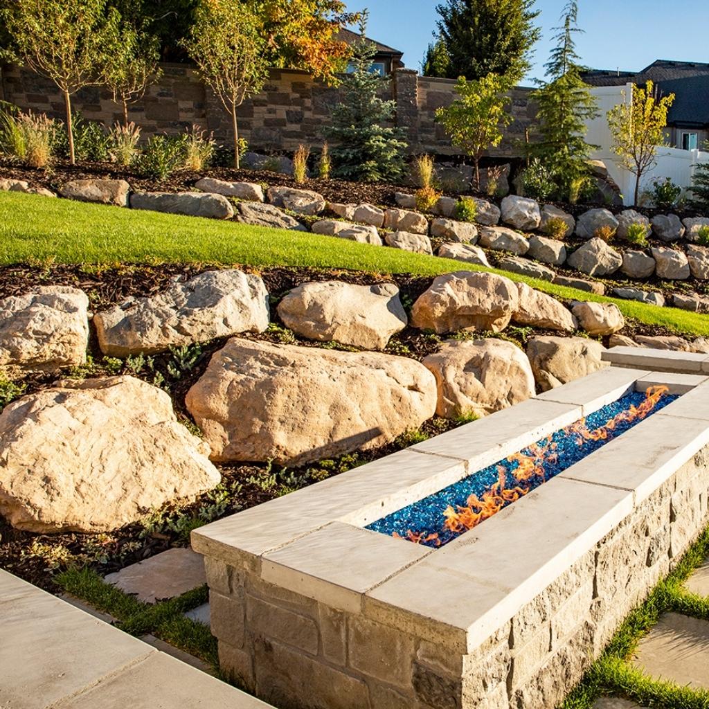 A well-manicured lawn bordered by natural rocks, featuring a rustic rock fire pit.