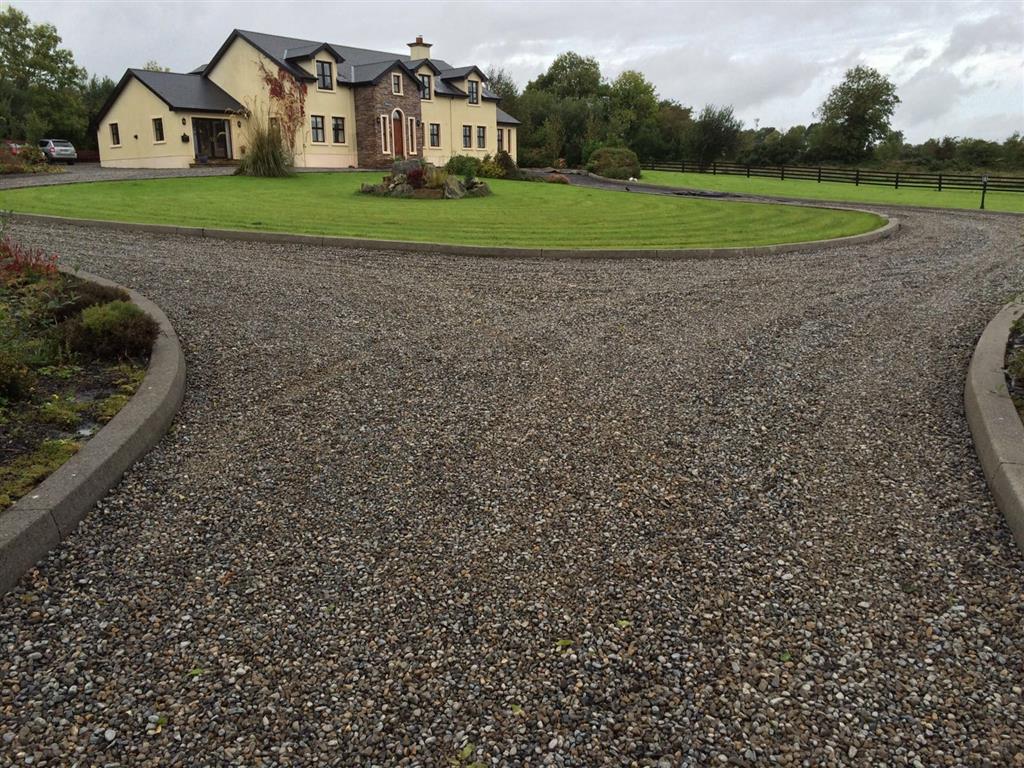 An inviting gravel driveway leading to a rustic country home, bordered by lush greenery.