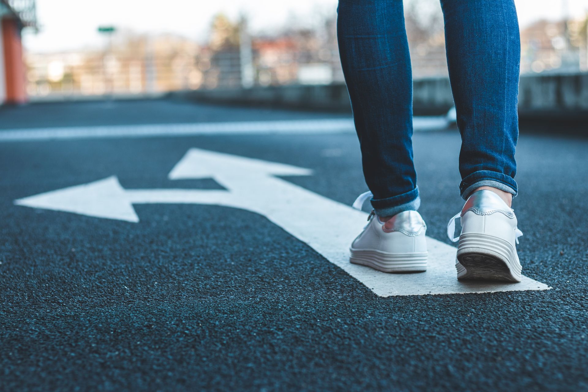 A person is walking on a white arrow on the road.