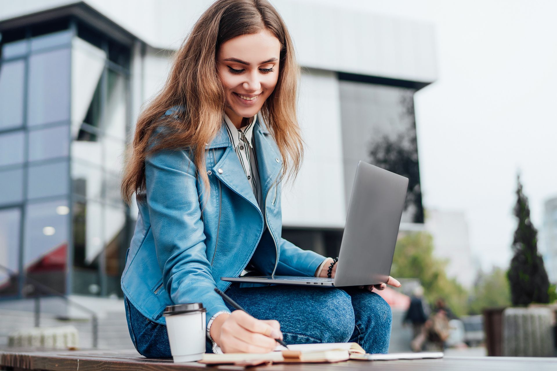 A woman is sitting at a table with a laptop and a cup of coffee.