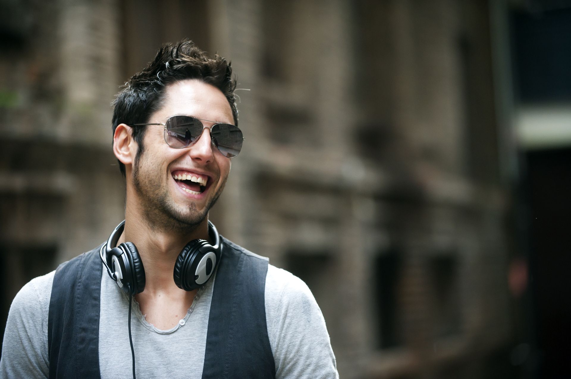 A man wearing headphones and sunglasses is smiling.