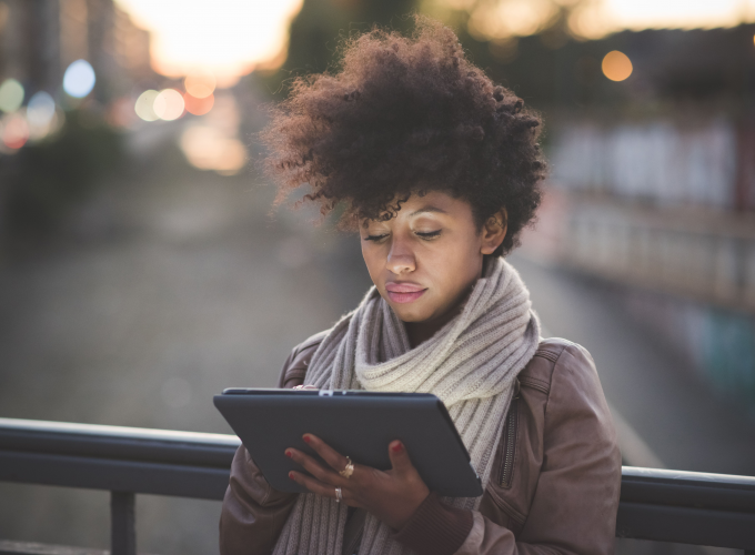 A woman is sitting on a bridge using a tablet computer.