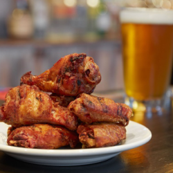 Pile of fried chicken wings on white plate, beer in glass behind.