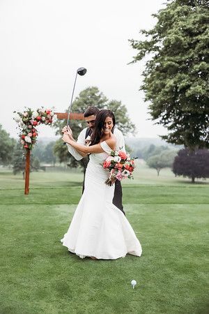 Bride and groom swing a golf club at their outdoor wedding.