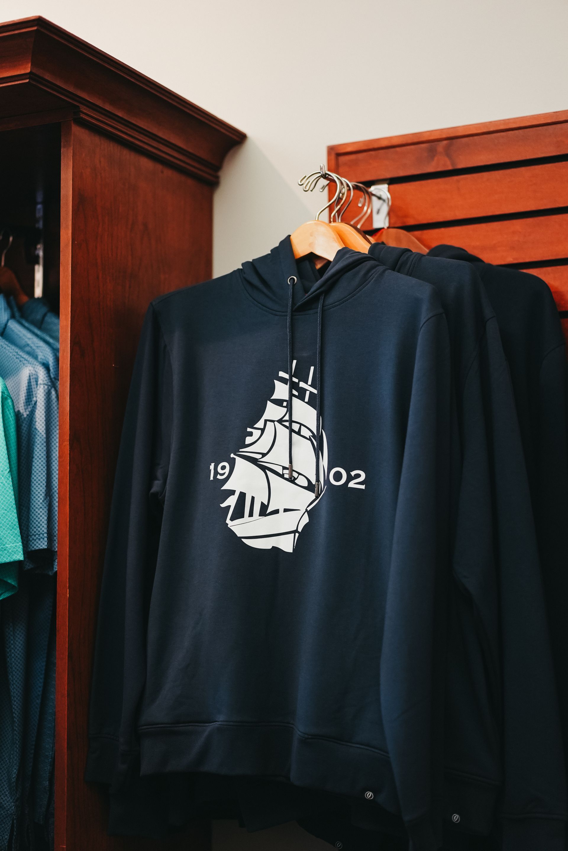 Navy blue hoodie with a white ship design hanging in a store.