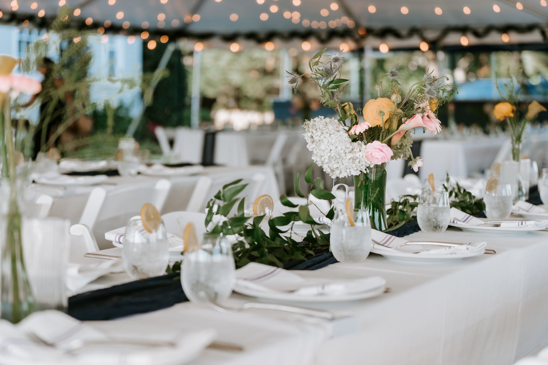 Elegant table setting with white tablecloth, floral centerpieces, and decorative glassware under a tent.