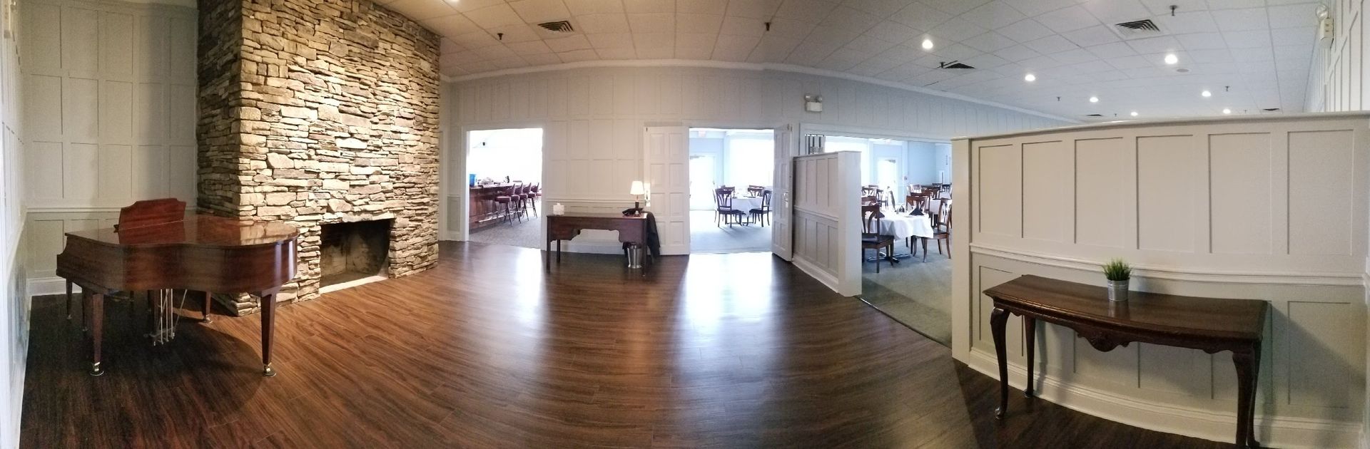 An empty banquet hall with a fireplace, piano, and tables. Wooden floors and white walls.