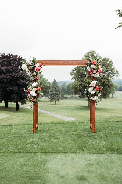 Wooden wedding arch decorated with red and white flowers on a golf course.
