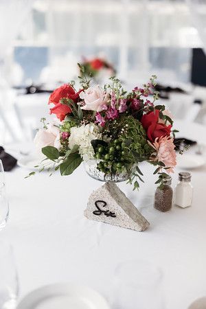 Centerpiece of roses and greenery on a white tablecloth, with a table number and salt/pepper shakers.