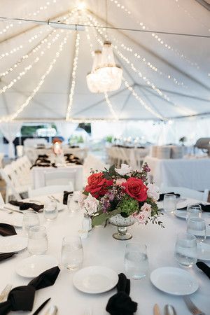 Table setting with red roses, under a white tent with string lights and a chandelier.