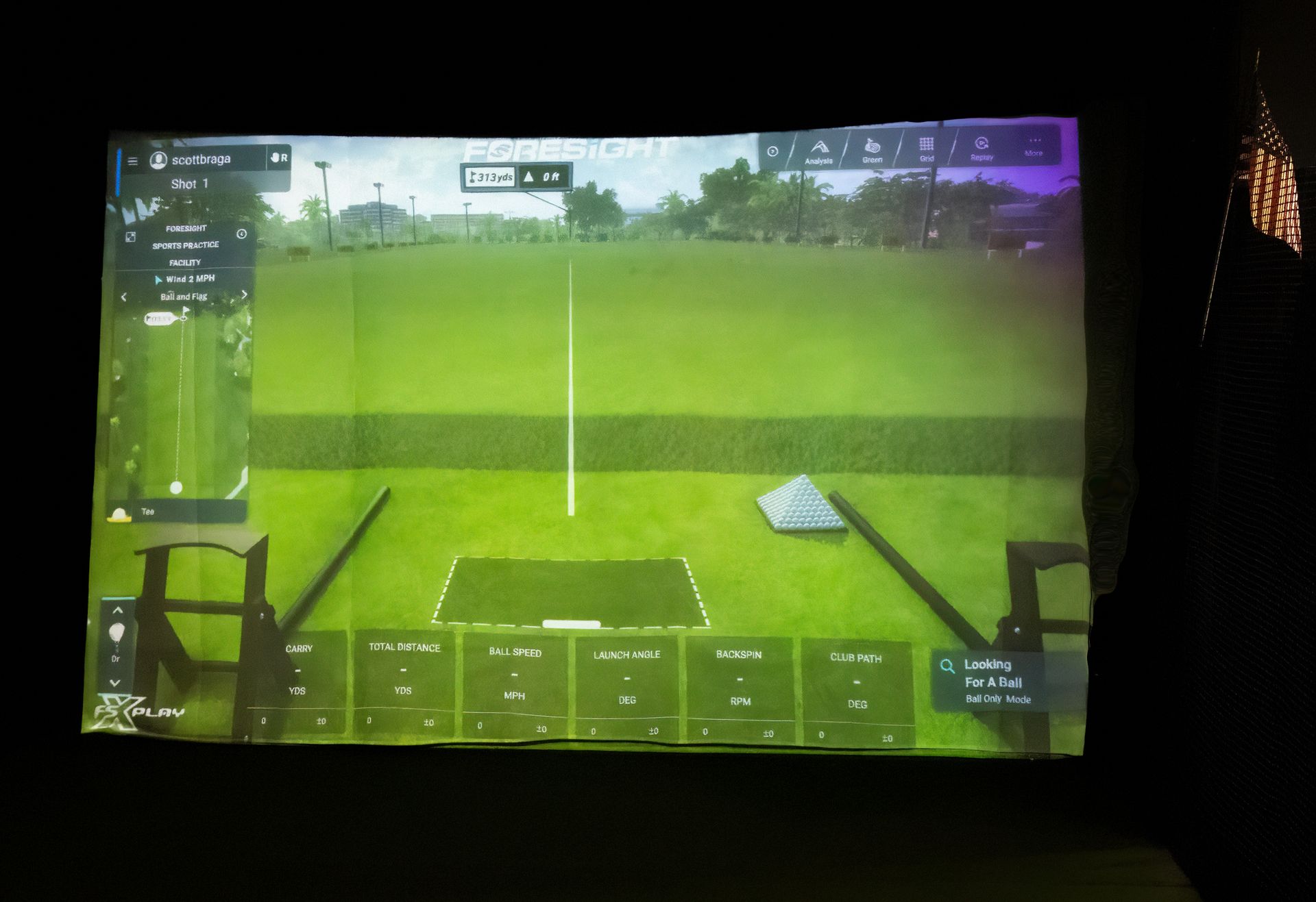 Person swings golf club in indoor simulator. Green screen displays course view, hitting a ball.