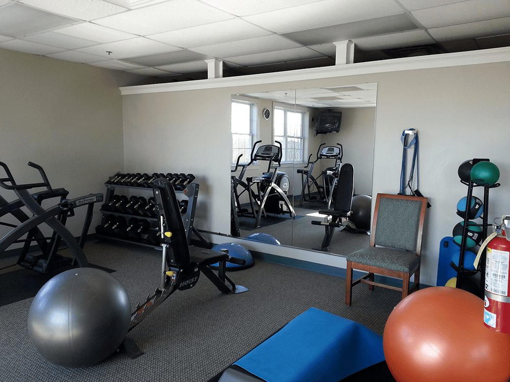 Gym with exercise equipment: weights, bikes, exercise balls, and a mirror.