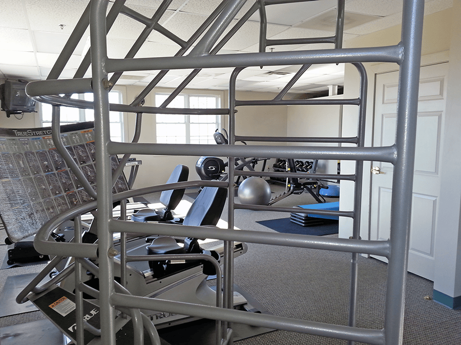 Gym with exercise equipment, including stair climber and weights; windows in background.