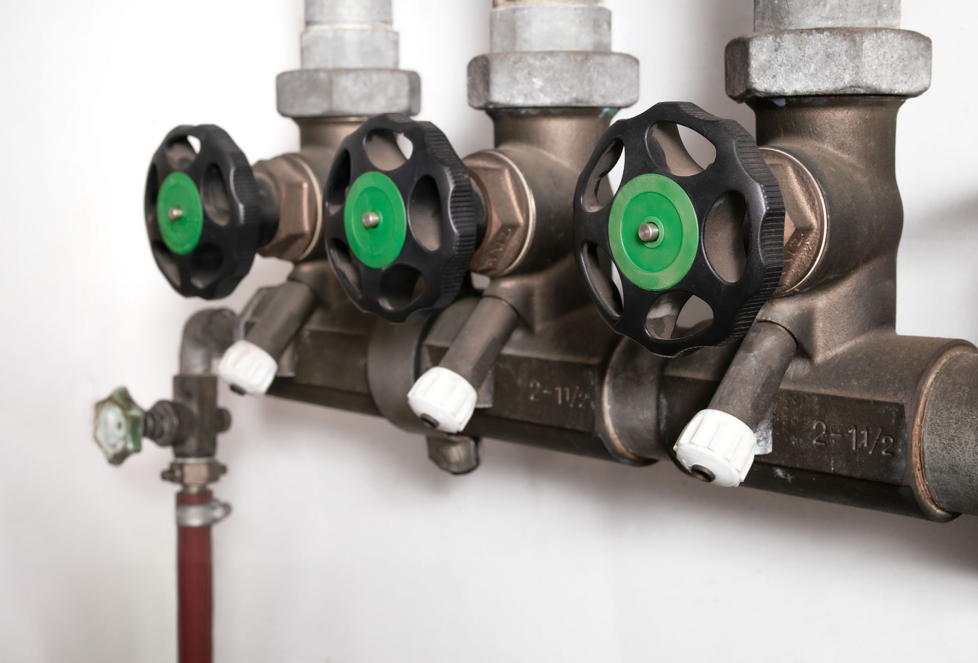 Three green valve knobs on a metal pipe manifold against a white wall
