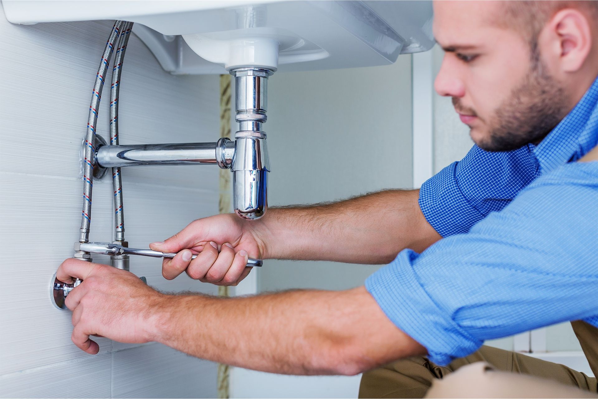 Plumber tightening a sink pipe under a bathroom basin with a wrench