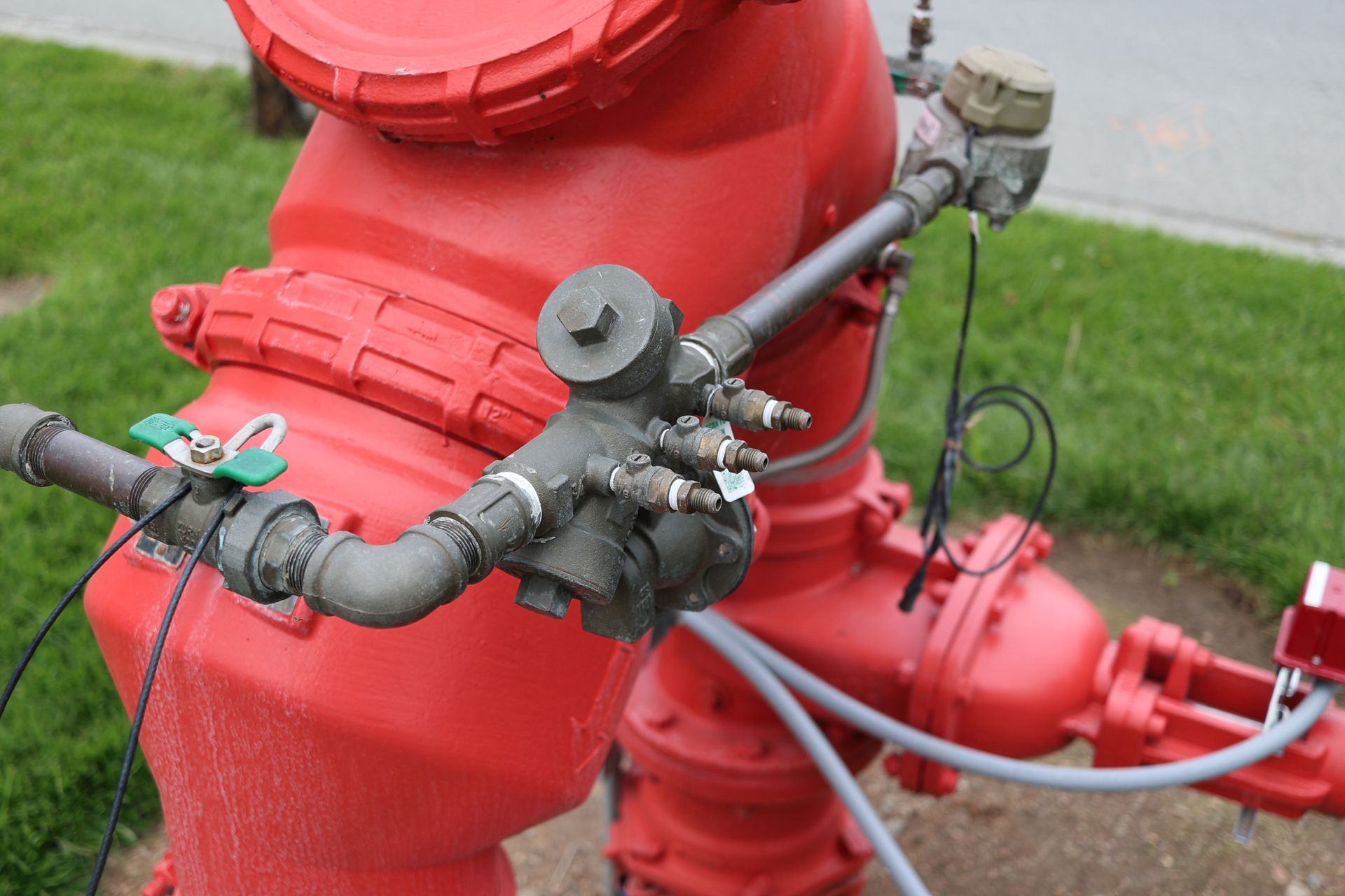 Red fire hydrant with attached black valves and pipes on a grassy roadside