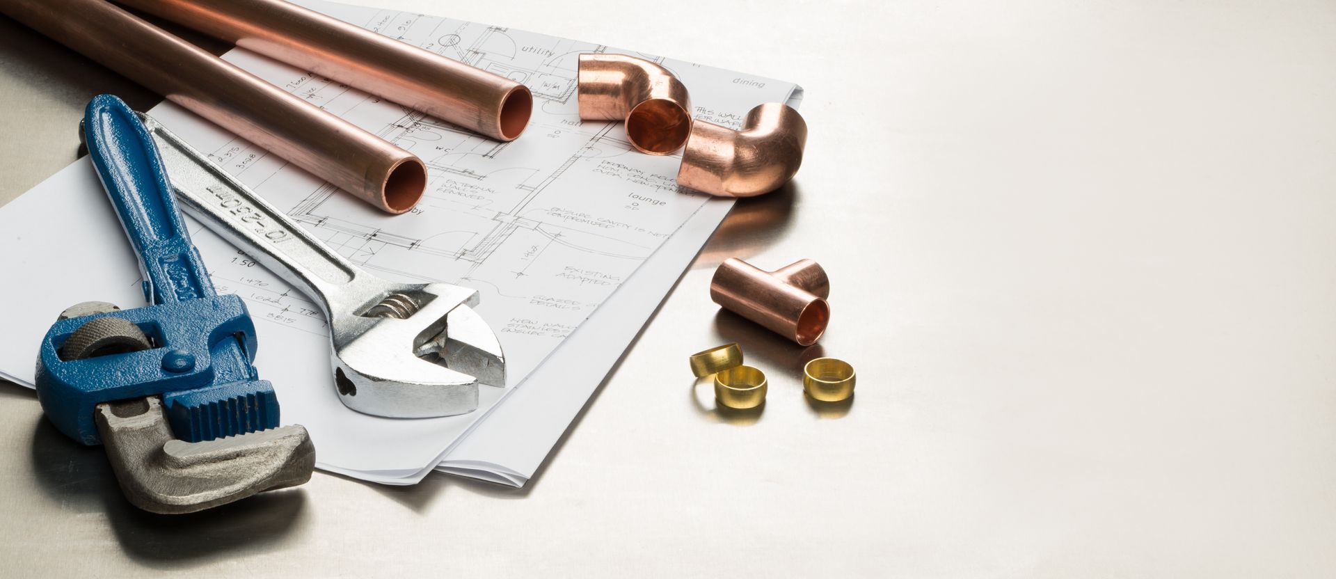 Pipes, fittings, wrench, and blue tape measure on a plumbing plan, with brass connectors on a white surface