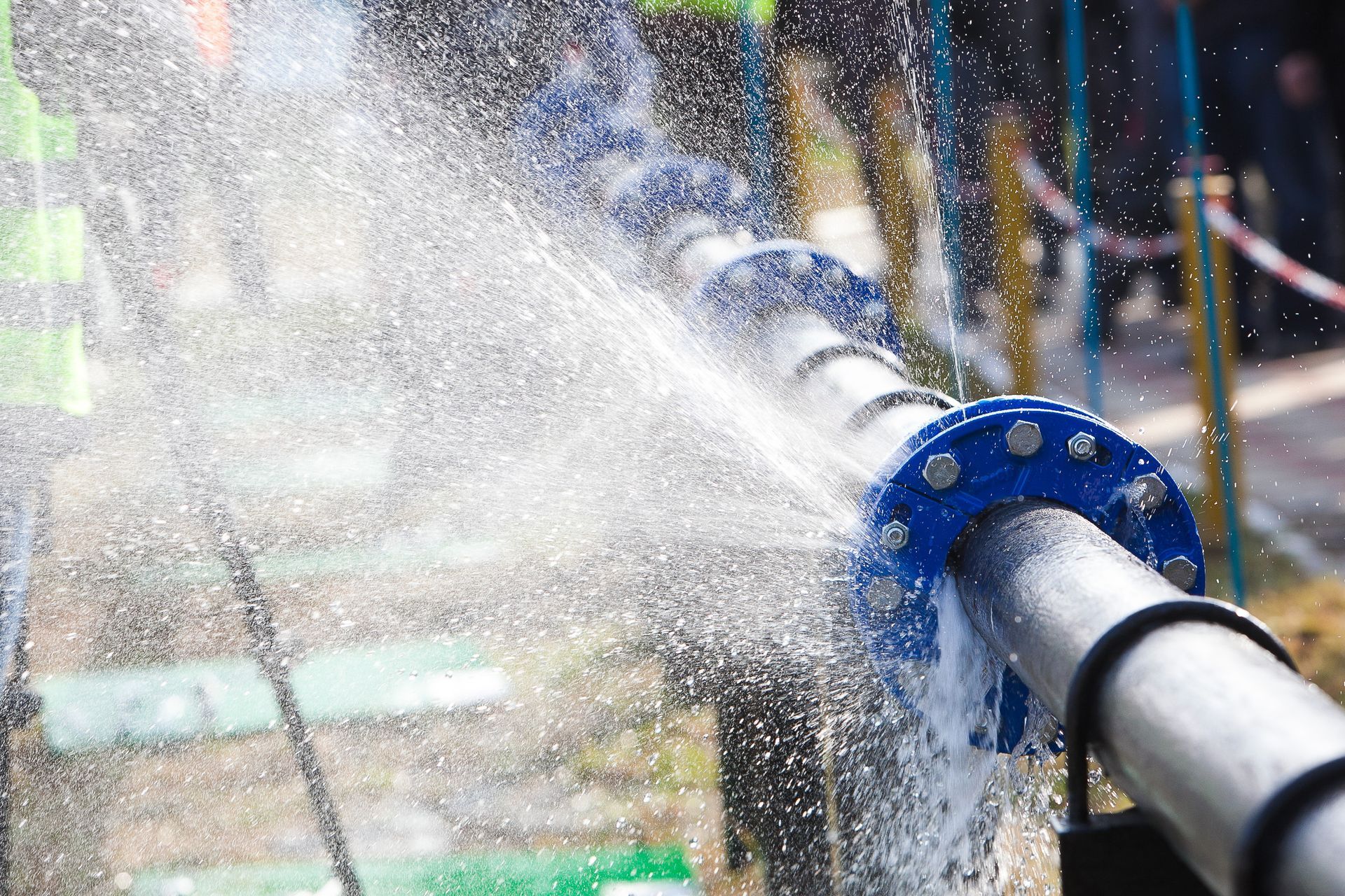 Water spraying from a metal pipe with a blue nozzle in an outdoor setting